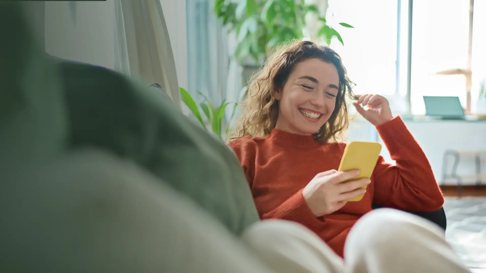 Happy relaxed young woman sitting on couch using mobile phone