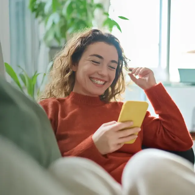 Happy relaxed young woman sitting on couch using mobile phone